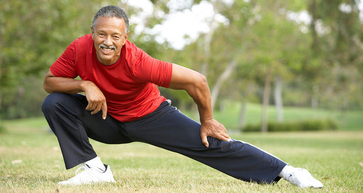 An older man in a red shirt doing a side lunge in a park
