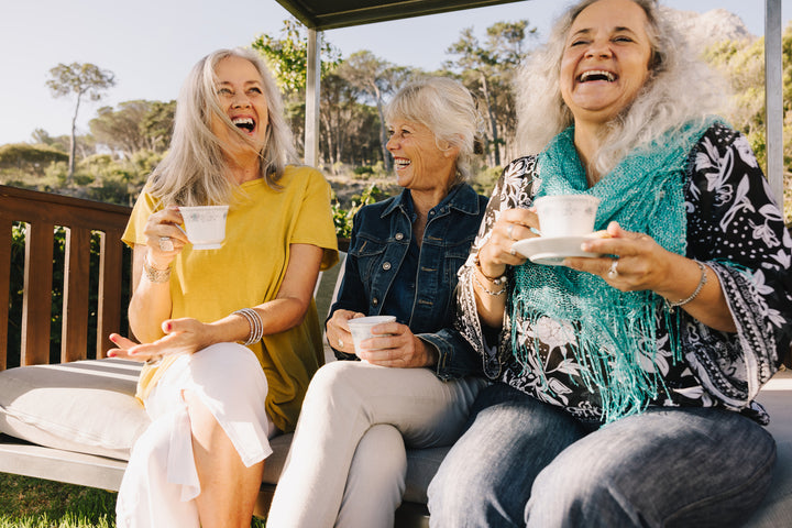 Three older women laughing and drinking coffee