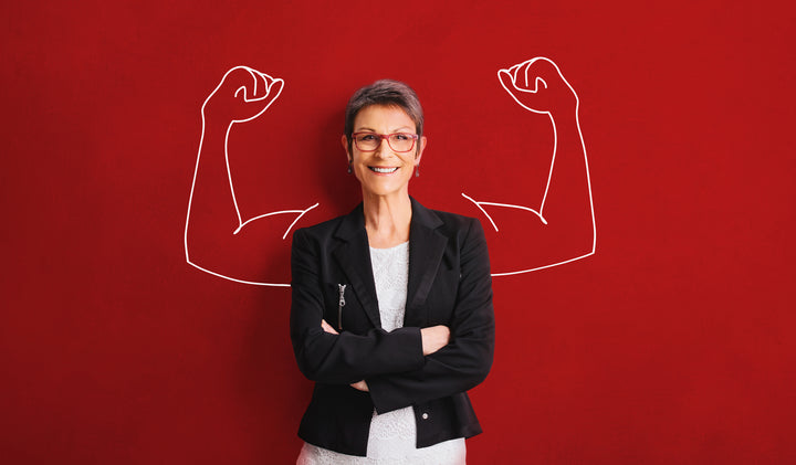 Woman standing against a red backdrop with drawn in arm muscles looking confident